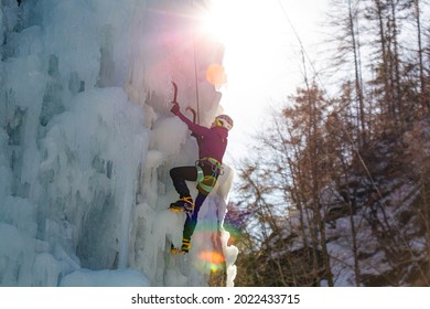 Female Ice Climber Hiking A Frozen Waterfall, Pushing Axe Pick Into The Slope And Moving Up To The Top