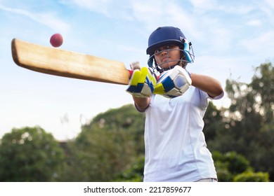 Female Indian cricket player wearing protective gear and hitting the ball with a bat on the field - Powered by Shutterstock