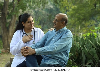 Female Indian Doctor Examining The Senior Patient Who Is Holding A Walking Stick In The City Park Afternoon. 