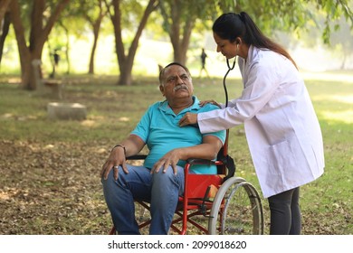 Female Indian Doctor Taking Care Of Senior Patient In Hospital Garden. The Patient Is Disable Of Walking And Getting Treated By A Specialist Family Doctor In The Fresh Air Atmosphere On Wheelchair.