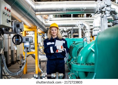 Female Industrial Engineer Standing By Gas And Oil Pipeline Inside Refinery.