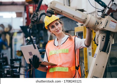 Female industrial engineer or technician worker in hard helmet and uniform using laptop checking on robotic arm machine. woman work hard in heavy technology invention industry manufacturing factory