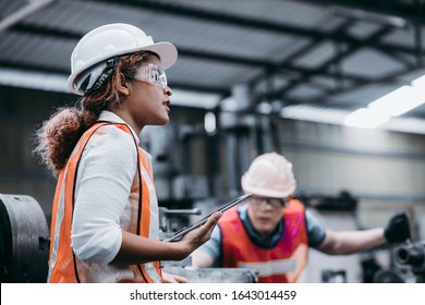 Female industrial engineer wearing a white helmet while standing in a heavy industrial factory behind she talking with workers, Various metal parts of the project - Powered by Shutterstock