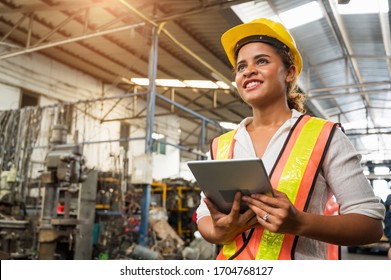 Female industrial worker working and checking machine in a large industrial factory with many equipment.