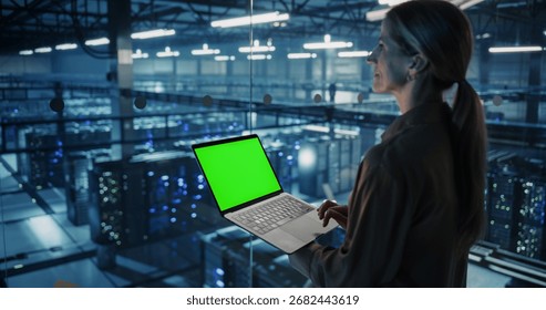 Female Information Technology Engineer Using Her Laptop Computer with Green Screen Chroma Key Display in a High-Tech Data Center, Analyzing Potential Risks to Ensure Network’s Safety and Compute Power
