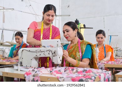 Female instructor explaining female textile worker by using digital tablet at factory