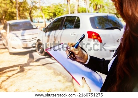 Female insurer working at the scene responsible for helping get car insurance during car crash junction taking notes documents evidence for inspection and claiming compensatiom disputing parties.