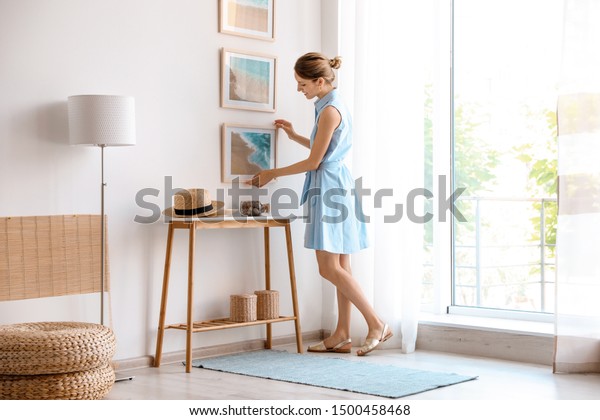 Female interior designer decorating white wall\
with pictures indoors