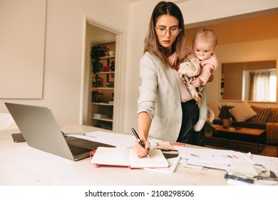 Female interior designer making notes while holding her baby. Multitasking mom planning a new project in her home office. Creative businesswoman balancing work and motherhood. - Powered by Shutterstock