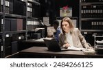 Female investigator entering workplace and sitting down to conduct forensic investigation on laptop. African american detective and caucasian police investigate case by looking at files and evidence.