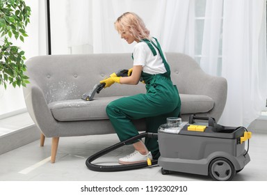 Female Janitor Removing Dirt From Sofa With Upholstery Cleaner In Room