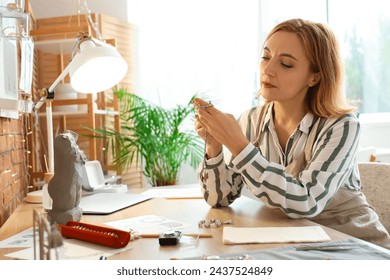 Female jeweler examining earring at table in workshop - Powered by Shutterstock