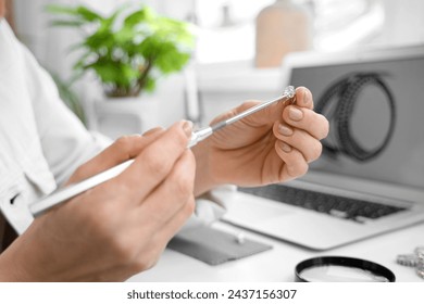 Female jeweler examining ring at table in workshop, closeup - Powered by Shutterstock