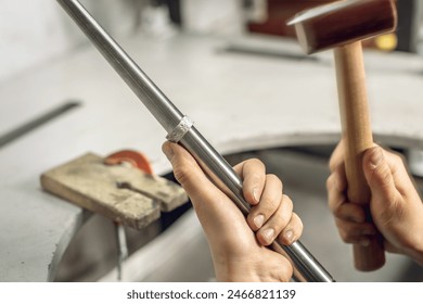 A female jeweler uses a hammer to align a piece of jewelry in the form of a silver ring. Craft in a jewelry workshop. - Powered by Shutterstock