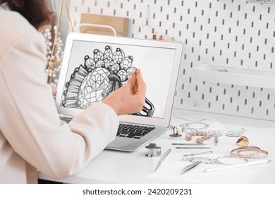 Female jewelry designer working with laptop and sketch of ring in office - Powered by Shutterstock