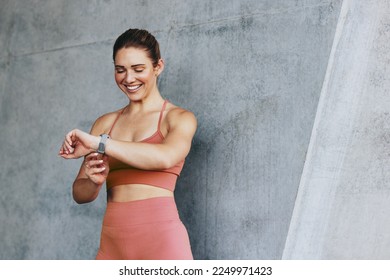 Female jogger checking her heart rate on a smartwatch after a run. Sports woman monitoring her progress with a fitness tracker. Happy woman doing a cardio workout outdoors. - Powered by Shutterstock