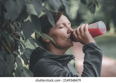 Female jogger drinking of refreshing strawberry juice in park, healthy lifestyle and recreational activity in 40s - Shutterstock ID 2149348479