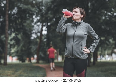 Female jogger drinking of refreshing strawberry juice in park, healthy lifestyle and recreational activity in 40s - Shutterstock ID 2149348485