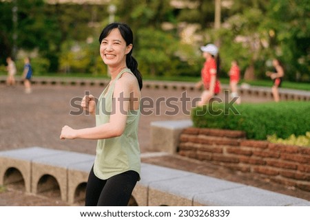 Female jogger. Fit Asian young woman with green sportswear aerobics dance exercise in park and enjoying a healthy outdoor. Fitness runner girl in public park. Wellness being concept