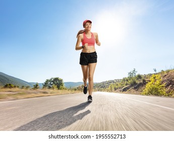 Female Jogger In Shorts Running On An Asphalt Road Towards The Camera 