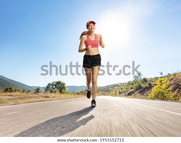Female jogger in shorts running on an asphalt road\
towards the camera 