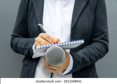 Female journalist at media event or news conference, writing notes, holding microphone. Journalism concept. - Shutterstock ID 1811048941