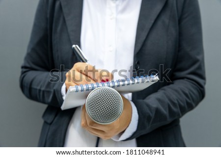 Female journalist at media event or news conference, writing notes, holding microphone. Journalism concept.