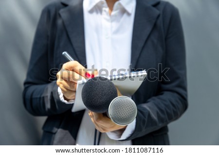 Female journalist at media event or press conference, writing notes, holding microphone. Journalism concept.