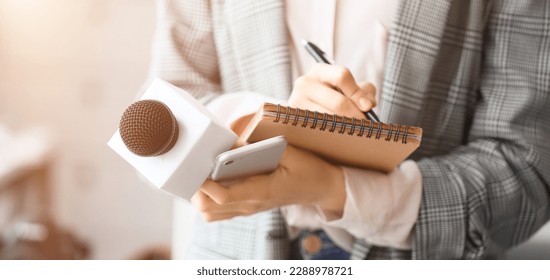 Female journalist with microphone, notebook and phone in office, closeup