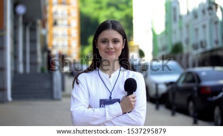 Female journalist with microphone and press pass looking at camera on street