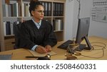 Female judge working at a desk in an office setting, wearing judicial robe with legal books in the background and scales of justice on the table