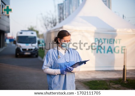 Female key doctor checking patient report form medical card,standing outside clinic exterior triage tent,Coronavirus COVID-19 illness diagnosis test,emergency due to global pandemic crisis,UK EMS Foto stock © 