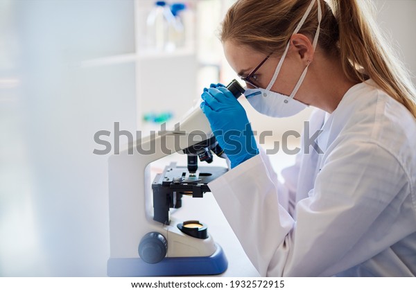 Female lab technician analyzing samples\
with a microscope while working at a table in a\
lab