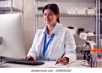 Female Lab Worker Wearing PPE Recording Blood Test Results On Computer