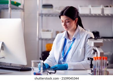 Female Lab Worker Wearing White Coat Recording Test Results On Computer