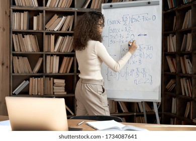 Female Latin Indian Math School Teacher Or Student Writing Equation On Whiteboard In Classroom. Virtual Live Remote Teaching Concept. Distance Online Education Exam Preparation Elearning Course.