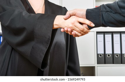 Female lawyer in black robe shakes hands with a client in her office - selective focus - Shutterstock ID 1569249793