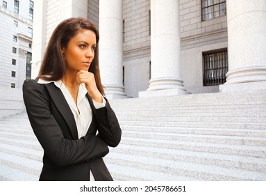 A Female Lawyer (or Business Person) Stands In Front Of A Courthouse Or Municipal Building Hand To Chin In Thought.