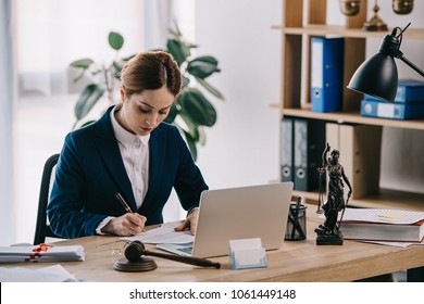 Female Lawyer In Suit At Workplace With Laptop, Gavel And Femida In Office