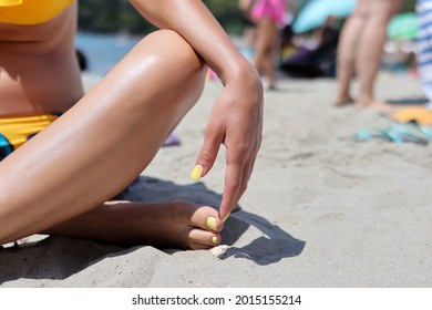 Female Leg With Yellow Pedicure On Feet And Hand On Knee. Women Sitting In Sea Sand On The Beach On A Summer Day. Close Up, Copy Space