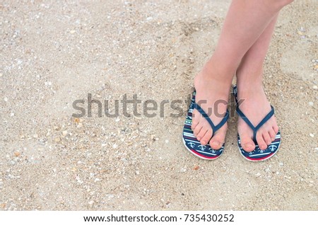 female legs in beach slippers on sea sand