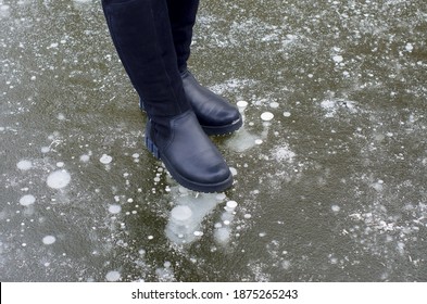 Female legs in black boots carefully walking on slippery road with frozen puddle covered with ice or thin ice of a pond. Concept of injury risk in winter and danger Dangerously slippery for pedestrian