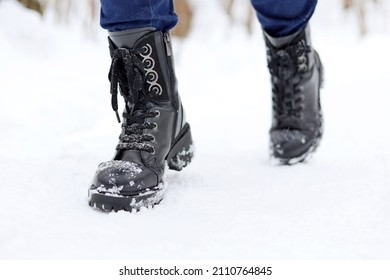 Female legs in black leather lace-up boots on a snow. Woman walking on winter street, warm footwear for cold weather