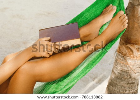 Female legs and book in the hammock on the beach