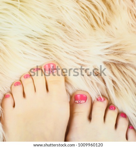 Female legs with a bright pedicure with rhinestones on the background of fur