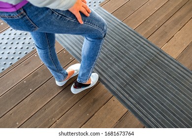 Female legs in denim jeans pants and light summer sneakers standing on wooden floow. - Shutterstock ID 1681673764
