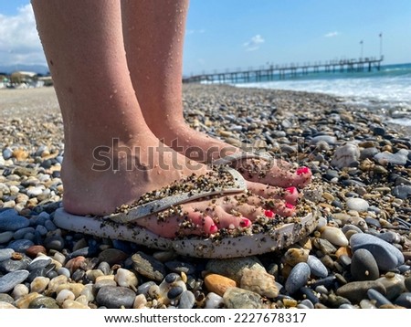 Female legs, feet in rubber slippers with a beautiful red pedicure on the background of sand on vacation on the beach in a warm tropical eastern paradise country southern resort.