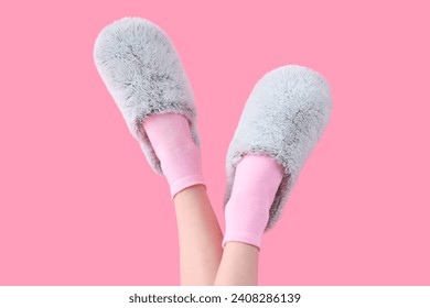 Patas femeninas con zapatillas suaves grises sobre fondo rosa