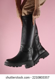 Female Legs In High Black Leather Boots On A Pink Background