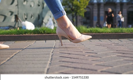 Female Legs In High Heels Shoes Walking Through Urban Street. Feet Of Young Woman In High-heeled Footwear Going In City. Unrecognizable Girl Stepping At Sidewalk. Side View Slow Motion Close Up